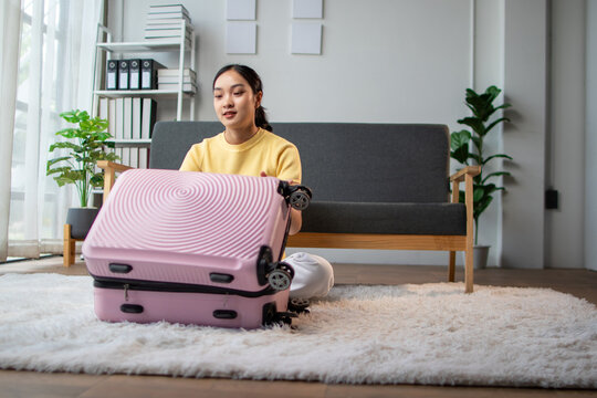 Young woman packing pink suitcase for travel trip at home.