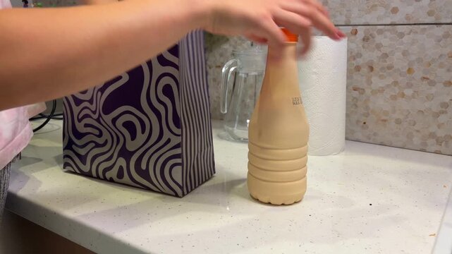 Person packing a thoughtful gift bag with a bottle of drink and a lunch box in the kitchen for a special surprise present for a friend or family member