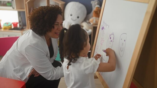 Woman teacher kneels beside little girl drawing on a whiteboard easel with purple marker in a classroom building, guiding her hand as she sketches faces; nurturing learning joy.