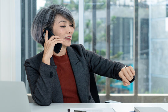 Businesswoman Checking Watch While on Phone Call in Office