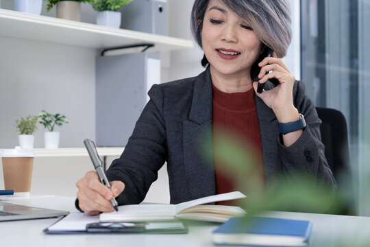 Businesswoman Taking Notes While on Phone Call in Modern Office