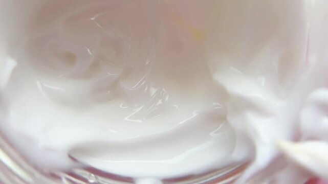 Close up view of stirring white cosmetic cream, demonstrating its smooth, thick, and viscous texture perfect for beauty care products and skincare advertising