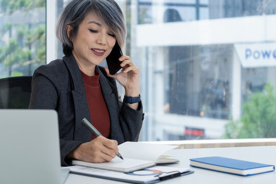 Businesswoman Taking Notes While on Phone Call in Modern Office