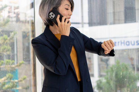 Businesswoman Checking Smartwatch on Phone Call by Office Window