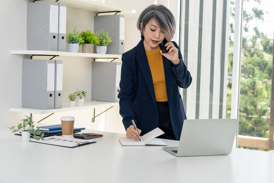 Multitasking Businesswoman Taking Notes on Phone Call in Office