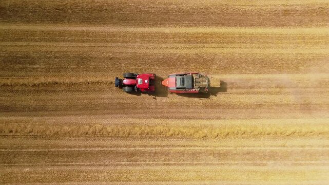 Aerial view of red square baler machinery baling straw on farmland after harvest