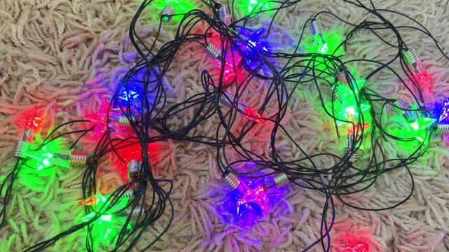 Flashing star shaped christmas lights glowing in festive red, green, and blue colors, creating a vibrant holiday atmosphere with tangled wires on a soft, fluffy carpet