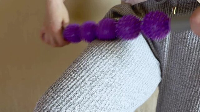 Woman massaging her leg with a purple spiky massage roller stick for myofascial release, muscle pain relief, and deep tissue stimulation to improve circulation at home