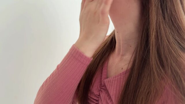 Young woman applying nourishing cream on her neck and jawline with gentle massaging motions against a white background for her daily skincare beauty routine