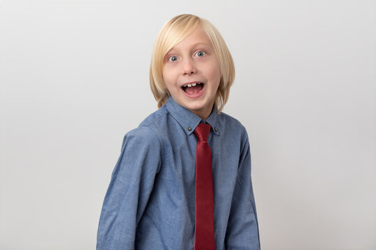 Young boy with blonde hair and a red tie looking directly at the camera with a wide open mouth, expressing surprise, joy, and a feeling of awe