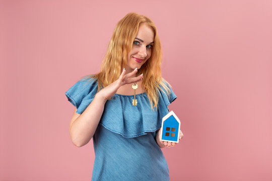 Young woman smiling at the viewer, holding a house model and a key, symbolizing new home ownership, real estate investment, and finding a perfect property