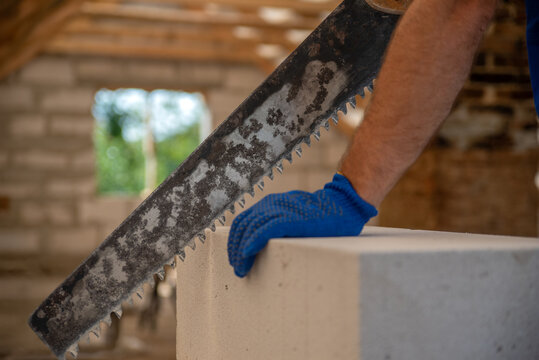 Construction worker's gloved hand carefully operating a large saw to cut a lightweight concrete block, demonstrating craftsmanship and building materials during home renovation