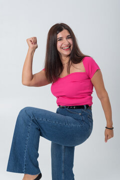 Young woman confidently celebrating an achievement, raising her arm and clenching her fist in a moment of strong excitement, happiness, and motivation on a clean white background