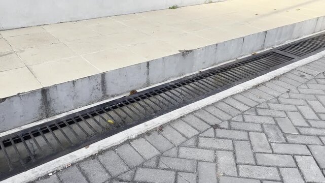Long iron drainage trench grate next to concrete curb on paving street