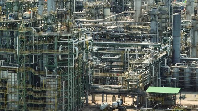 An aerial perspective of a large oil refinery with complex pipelines, towers, and chemical processing facilities representing heavy industry, operational efficiency, fossil fuel transition challenges.