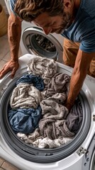 Obraz premium A man loads colorful laundry into a front-loading washing machine, with the spinning drum visible in the background.