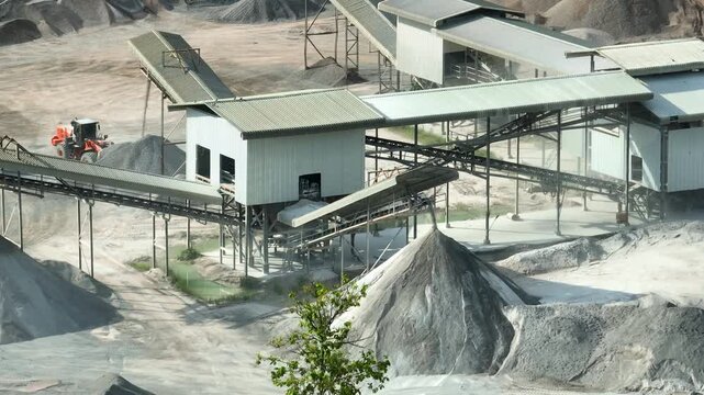 An aerial capture of a quarry processing facility featuring geometric conveyor networks and aggregate piles, representing mineral extraction, construction supply chains, industrial development.
