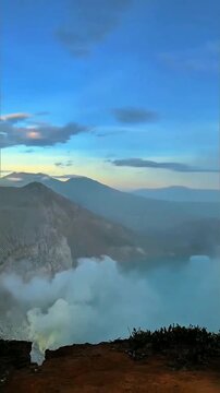 Dense lush green forest blankets layered hills, thick white mist drifts through deep valleys under soft pale sky with far mountain silhouettes