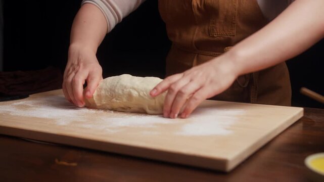 Close-up of hands shaping soft bread dough into a smooth round loaf on a floured wooden board. Traditional homemade baking process with fresh dough ready for proofing.