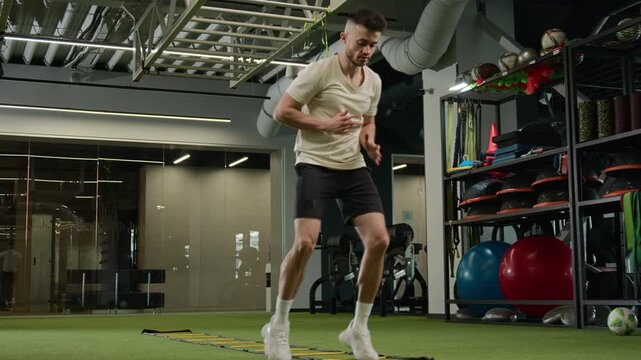 Caucasian footballer man player training with agility ladder in sports gym soccer athlete male sportsman performing cardio workout jumping exercise speed coordination match fitness equipment endurance