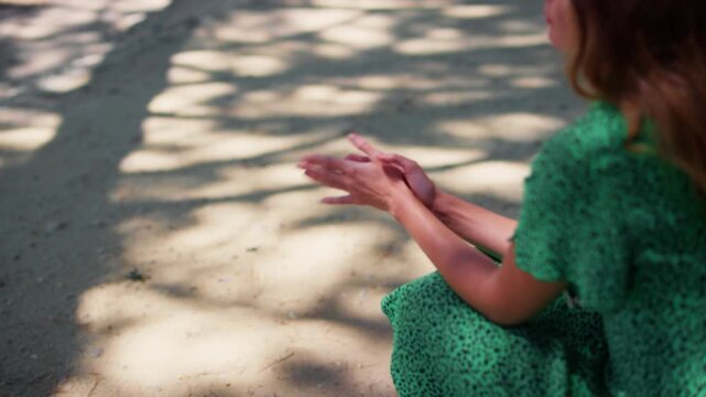 Side profile of woman in green leopard print dress outdoors with hand gesture beneath sunlit dappled shadows