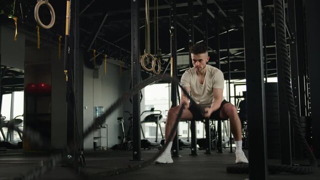 Muscular athlete Caucasian man making waves with battle ropes in gym sportsman strong male functional workout exercise sport equipment intense training strength endurance cardio bodybuilding challenge