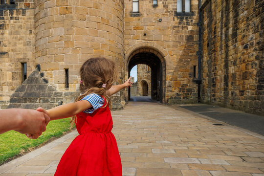 Girl in red dress joyfully lead adult through castle courtyard