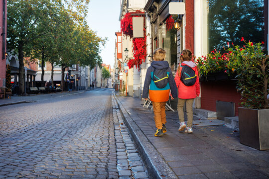 Two children travel with backpacks walk along cobblestone street