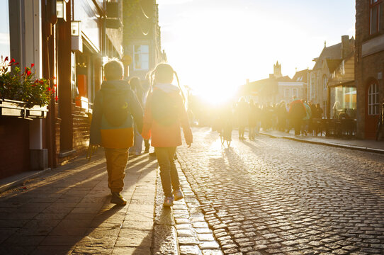 Two children walk along sunlit cobbled street in town center