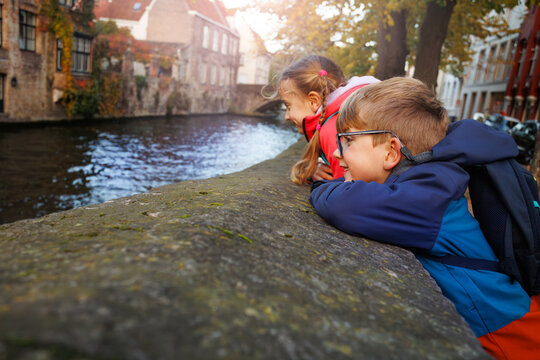 Two kids look over canal wall in cobbled Bruges streets, Belgium