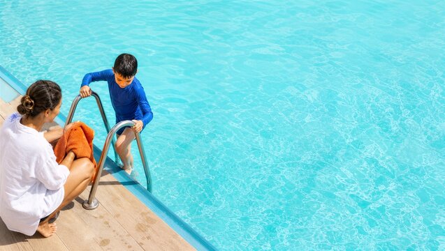 Woman watching boy climbing out of pool with ladder. Mother holding orange towel on wooden deck. Summer vacation, family fun, swimming safety concept