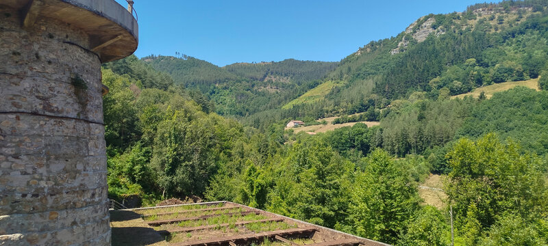 Paisaje monta&ntilde;oso verde con &aacute;rboles y peque&ntilde;a casa rural bajo cielo azul