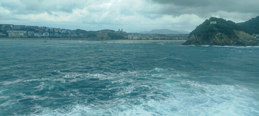 Fototapeta premium Vista panorámica de la bahía y la costa marítima bajo cielo nublado en San Sebastián, España.