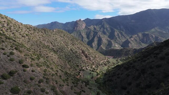 An aerial boom up and push in drone movement towards Roque Cano with Vallehermoso below on La Gomera (Canary Islands)