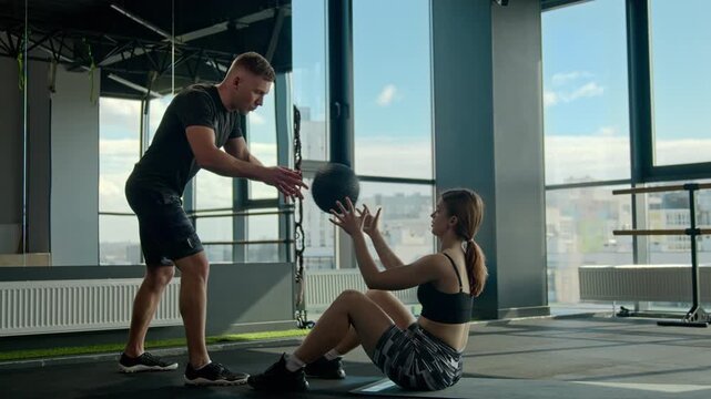 Caucasian sportswoman training with male trainer athlete throwing medicine ball inside gym muscular fitness couple family doing sit ups workout bodybuilders exercise cardio healthy lifestyle teamwork