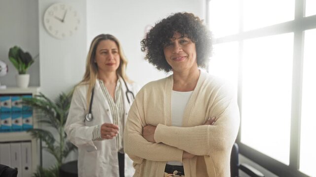 Woman patient with arms crossed and doctor wearing white coat and stethoscope placing hand on shoulder in clinic building; supportive care reassurance.