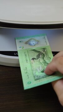 Examination of malaysian ringgit (MYR) cash money with UV counterfeit detector. Concept of authenticity check, fight against counterfeiting of banknotes, anti fraud measures in Malaysia. Close up view