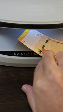 Examination of malaysian ringgit (MYR) cash money with UV counterfeit detector. Concept of authenticity check, fight against counterfeiting of banknotes, anti fraud measures in Malaysia. Close up view