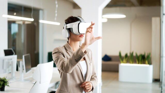 Close up portrait of Caucasian pretty young businesswoman working in modern office wearing VR headset moving hands in air. Female works on a project using virtual reality glasses. Metaverse concept
