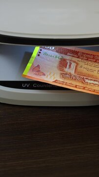 Examination of Sri Lanka rupee (LKR) cash money with UV counterfeit detector. Concept of authenticity check, fight against counterfeiting of banknotes, anti fraud measures in Sri Lanka. Close up view.