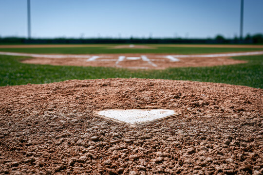 A close-up view of home plate on a baseball field with the pitcher's mound and bases visible in the distance under a clear blue sky.