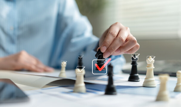 Business hand moving chess piece with approval check icons over financial documents, representing strategic planning, decision making, leadership, business success, management and risk assessment.