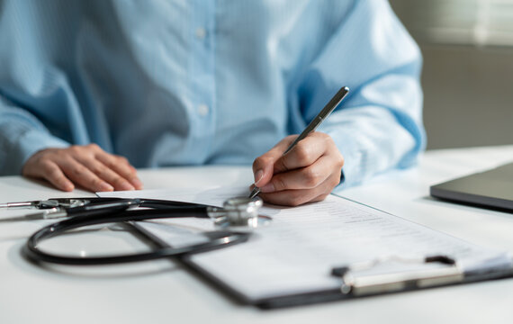 Healthcare professional completing medical documents beside a stethoscope, representing patient records, healthcare administration, medical documentation, insurance claims and clinical services.