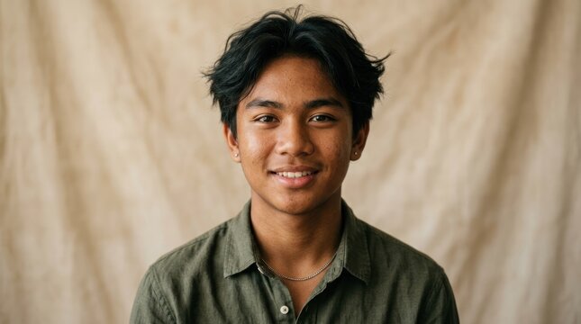 A young man with dark hair wearing a green shirt, standing against a beige background with a neutral expression.