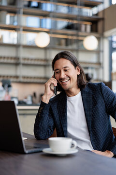 Smiling man on phone with laptop and coffee.