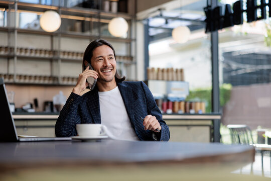 Smiling man on mobile phone with laptop and coffee.