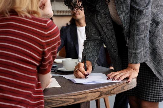 Business meeting, woman signs document, colleagues observe.