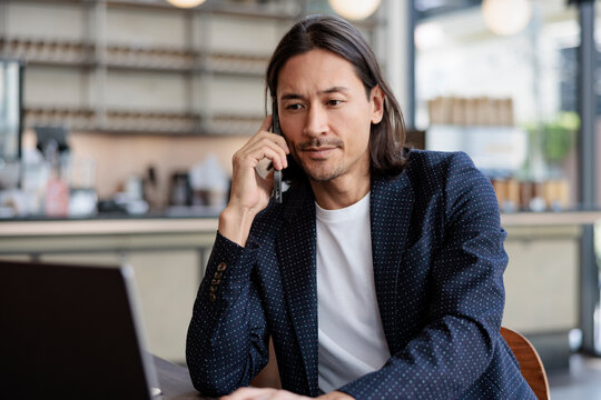 Man talking on mobile phone with laptop in cafe setting.