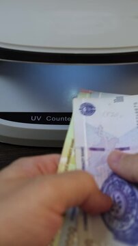 Examination of Uzbekistan Sum (UZS) cash money with UV counterfeit detector. Concept of authenticity check, fight against counterfeiting of banknotes, anti fraud measures in Uzbekistan. Close up view.