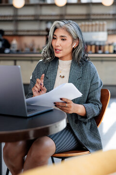 Professional woman reviews documents during a virtual meeting in cafe